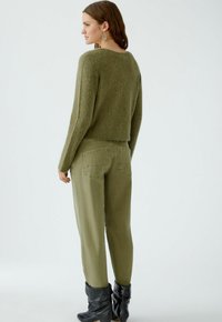 Olivgrüner Pullover mit cropped Design und strukturierter Verarbeitung, kombiniert mit olivgrünen, hochgeschnittenen Hosen mit Gesäßtaschen und lockerer Passform.