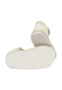 Zapato de cuña beige con parte superior de tela texturizada, correa ajustable y suela de goma estriada para mayor tracción. Presenta un patrón floral sutil.