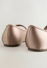 Ballerine in satin rosa chiaro con punta arrotondata e parte posteriore. Presentano una sottile cinturino e una cucitura discreta lungo il bordo. Suola in gomma piatta.