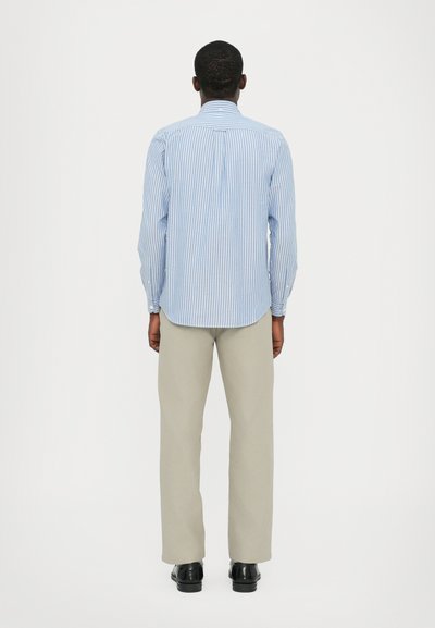 Camisa a rayas azul claro y blanca con mangas largas y cuello, combinada con pantalones beige y zapatos negros, vista desde la espalda.