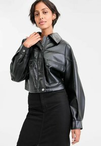 Giubbotto in pelle nera tagliato, con colletto, chiusura a bottone e due tasche frontali. La texture liscia e il design sartoriale enfatizzano uno stile moderno.