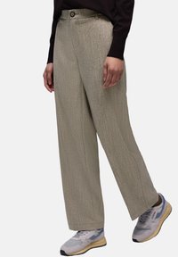 Beige strukturierte Schlaghosen mit geradem Schnitt, ausgestattet mit Knopfverschluss und vorderen Taschen, kombiniert mit grauen und gelben Sneakers.