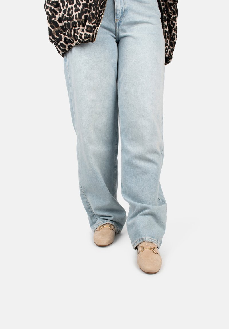 Lichtblauwe, hooggewaisted jeans met een relaxte pasvorm, gecombineerd met tan suède loafers met gouden hardware accenten. Luipaardprint jas gedeeltelijk zichtbaar.