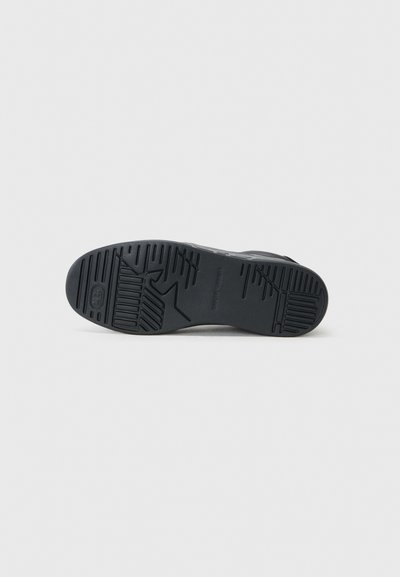 Suela de zapato de goma negra con un patrón de agarre texturizado, con surcos y marcas, diseñada para ofrecer tracción y estabilidad.