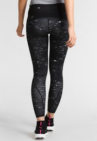 Zwarte leggings met een draaiend wit patroon, voorzien van een hoge tailleband en contrasterende stiksels. G gedragen met zwarte sneakers en roze accenten.