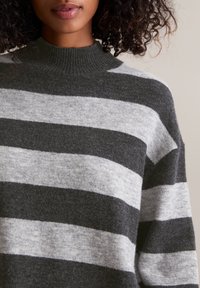 Pull rayé gris et gris clair avec un col côtelé haut, fabriqué en tissu doux et texturé. Focus visuel sur la partie supérieure de la poitrine.