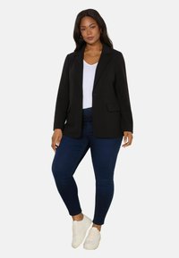 Black blazer with notch lapels, single button closure, and side pockets, paired with a white t-shirt and dark blue skinny jeans. White sneakers.