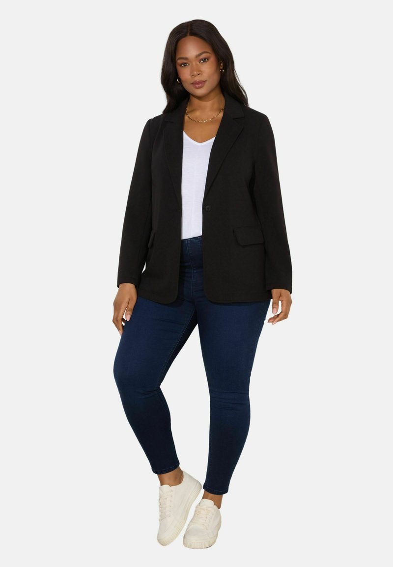 Black blazer with notch lapels, single button closure, and side pockets, paired with a white t-shirt and dark blue skinny jeans. White sneakers.