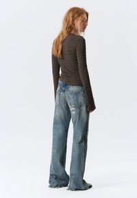 Gestreiftes langärmliges Oberteil in Braun und Creme, kombiniert mit ausgebleichten blauen, weit geschnittenen Jeans mit verwaschenen Akzenten und einem Fünf-Taschen-Design.