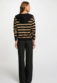 Maglione a righe nero e oro con cappuccio, maniche lunghe e polsini a coste, abbinato a pantaloni neri a vita alta.