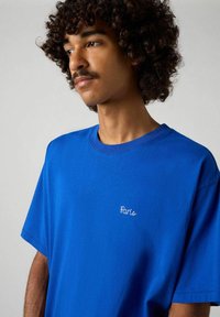 Camiseta de algodón azul con mangas cortas, escote redondo y detalle bordado "París" en el pecho. Textura suave y corte relajado.