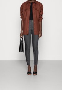 Brown button-up shirt with two chest pockets, paired with gray fitted pants. Black handbag and open-toe black heels complete the outfit.