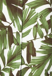 Couture avec points visibles sur un tissu imprimé de feuilles de palmier vertes superposées sur un fond blanc.