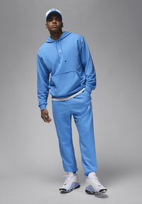 Felpa azzurra e pantaloni della tuta coordinati, realizzati in tessuto morbido, con un logo sul petto e sui pantaloni. Scarpe da ginnastica bianche con accenti.