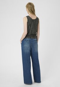 Grijze, gestructureerde mouwloze top gecombineerd met wijde, vervaagde blauwe denim jeans. De top heeft een ronde rug en subtiele details.