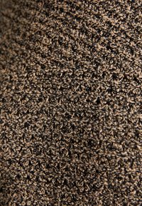Tessuto testurizzato in tonalità di nero e beige, con un motivo lavorato a maglia che presenta un mix di filamenti morbidi e lisci.