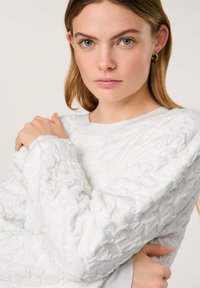 Weißer, strukturierten Sweatshirt mit einem zerknitterten Muster, rundem Halsausschnitt und langen Ärmeln. Weicher Stoff mit lockerer Passform. Minimalistisches Design.