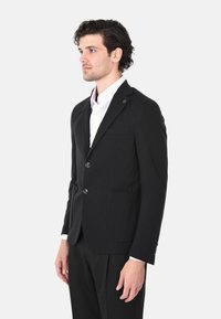 Blazer nero con due bottoni, revers a punta e taschino sul petto. Combinato con una camicia bianca, dalla vestibilità su misura e design minimalista.