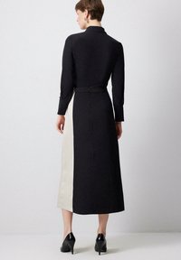 Robe longue avec un haut noir et un panneau latéral beige, fabriquée dans un tissu lisse. Comprend un col, des manches longues et une fermeture éclair.