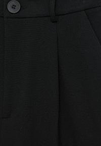 Pantalon noir sur mesure avec fermeture à bouton, passants pour ceinture et poche en couture latérale visible.