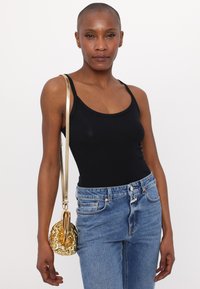 Bolso metálico dorado con superficie texturizada y correa de cadena, combinado con una camiseta sin mangas negra y pantalones vaqueros de tiro alto azul.
