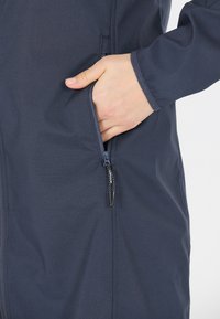 Marinblå ytterficka med dragkedja med en hand inuti, med en slät tygtextur och en enkel design. Dragkedjans drag har en dekorativ detalj.