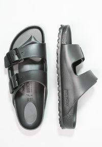 Sandales Birkenstock noires avec deux sangles réglables, fabriquées en matériau synthétique lisse, dotées d'une semelle intérieure ergonomique et d'une semelle extérieure texturée.