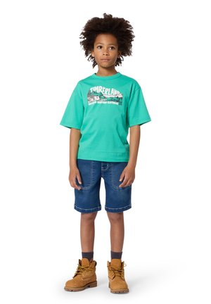 Turquoise T-shirt met korte mouwen en een grafisch ontwerp, gecombineerd met denim shorts en bruine wandelschoenen. Textuurstof en losse pasvorm.