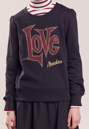 Sweat-shirt bleu marine avec un grand texte rouge et or "LOVE" et le logo "Moschino", porté sur un col roulé rayé blanc, rouge et bleu marine.