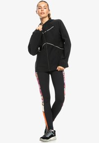 Black zip-up jacket with reflective accents, paired with form-fitting black leggings featuring a colorful floral pattern and orange detailing.