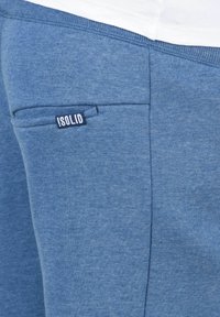I joggers blu in cotone presentano una finitura testurizzata sottile, una tasca laterale con una piccola etichetta bianca e nera che recita “!SOLID.” Dettaglio con elastico in vita.