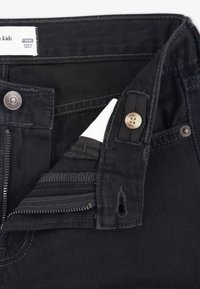 Crne traperice od denima s metalnim gumbom i zatvaračem na zip. Sadrže ušivenu oznaku i tekstilnu petlju. Glatka tekstura i regularni kroj.