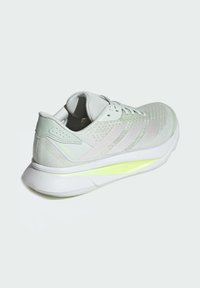 Lichtgrijze hardloopschoen met een ademende bovenkant van mesh, witte tussenzool en een neon groene accent op de hak met de tekst 'LIGHTMOTION'.