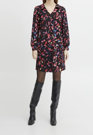 Musta mekko, jossa on värikäs abstrakti kuvio punaisena, vaaleanpunaisena, sinisenä ja keltaisena. Varusteena pitkähihaiset hihat ja V-pääntie, yhdistettynä kiiltäviin mustiin polvenkorkuisiin saappaisiin.