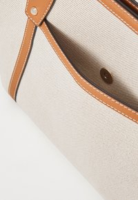 Beige vászontáska barna bőrkiegészítőkkel, mintás szövettel, kontrasztos varrással és arany színű patent zárral.