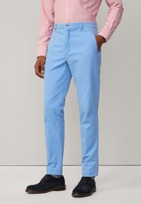 Pantalons en coton bleu clair avec une coupe slim, dotés de poches latérales, d'une fermeture à bouton et d'une texture lisse, associés à des chaussures foncées.