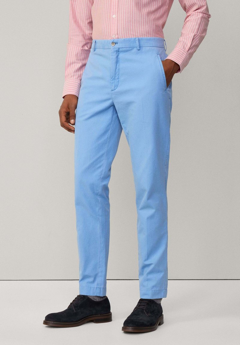 Pantalons en coton bleu clair avec une coupe slim, dotés de poches latérales, d'une fermeture à bouton et d'une texture lisse, associés à des chaussures foncées.