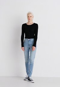 Fekete, hosszú ujjú, testhez álló felső, kerek nyakkivágással és gombos részletekkel, világoskék, skinny farmernadrággal és fekete sportcip�ővel párosítva.