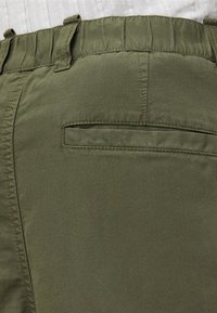 Shorts vert olive avec un tissu texturé, dotés d'une taille froncée et d'une petite poche arrière. Le design est simple et fonctionnel.