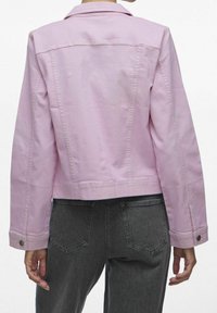 Chaqueta de mezclilla rosa con un diseño corto, puños abotonados y costuras en la parte posterior. Combinada con vaqueros gris de talle alto que presentan dos bolsillos traseros.