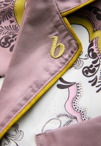 Haină de mătase cu exterior roz și accente galbene, decorată cu modele florale. Pe guler se află o mică literă "b" galbenă brodată.