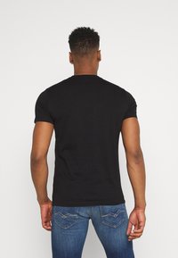 Czarna bawełniana koszulka z krótkimi rękawami i okrągłym dekoltem, w zestawie z niebieskimi dżinsami z charakterystycznym haftowanym wzorem kieszeni.