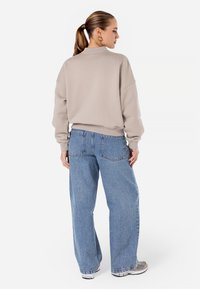 Beige oversized genser med ribbestrikket hals, kombinert med lyseblå baggy jeans med baklommer og en avslappet passform.