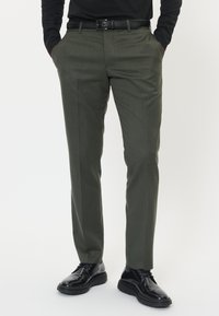 Olivgrön skräddarsydda byxor i texturerad tyg, med slim fit, framfåra och sidofickor, kombinerade med svarta finskor.