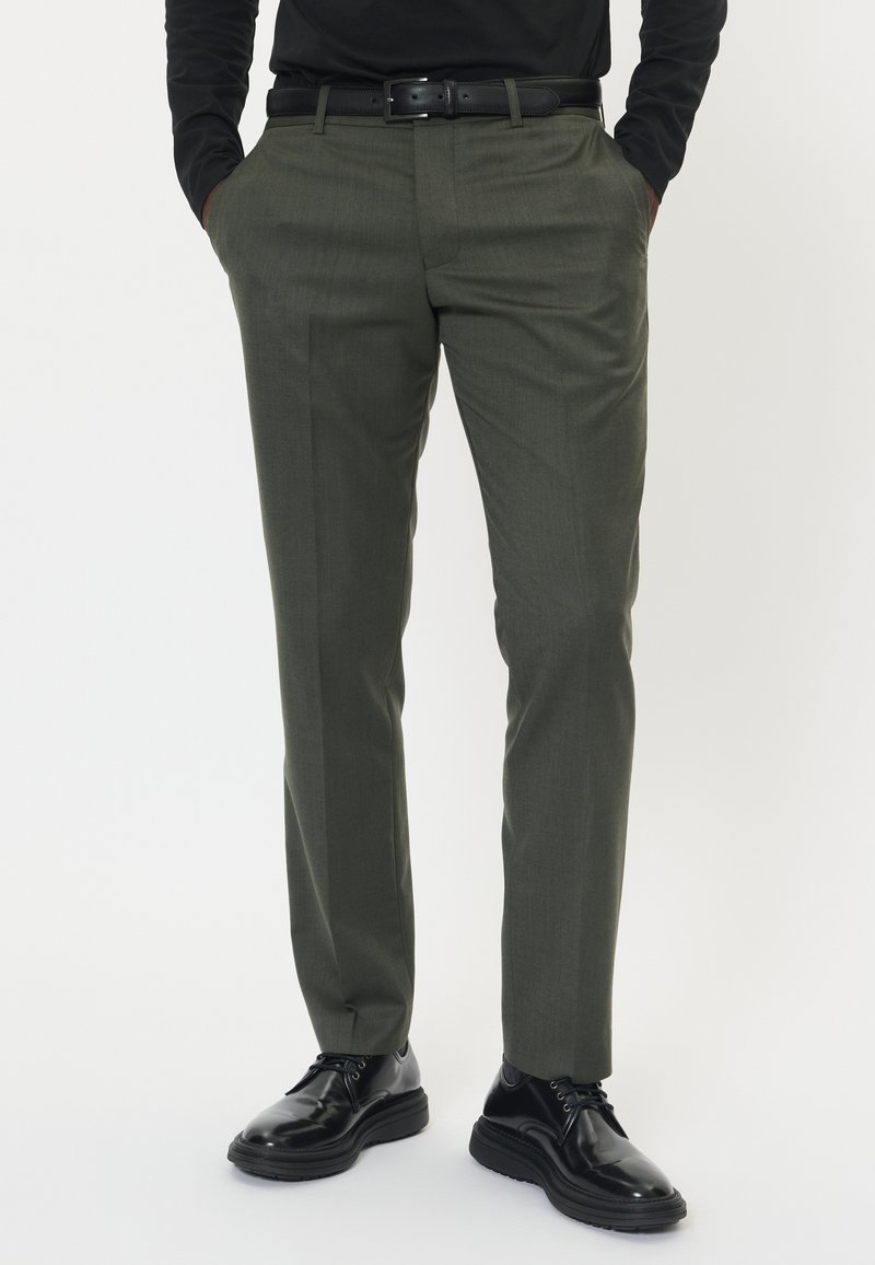 Olivgrön skräddarsydda byxor i texturerad tyg, med slim fit, framfåra och sidofickor, kombinerade med svarta finskor.