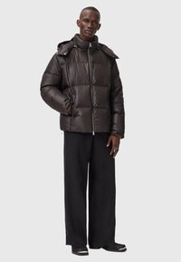 Polstret sort jakke med høj krave, frontlynlås og sidelommer; har en hætte og quiltet design. Sammen med løse sorte bukser.