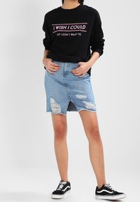 Černá mikina s růžovým textem, v kombinaci se světle modrou vybledlou džínovou sukní s předním rozparkem a černými teniskami.