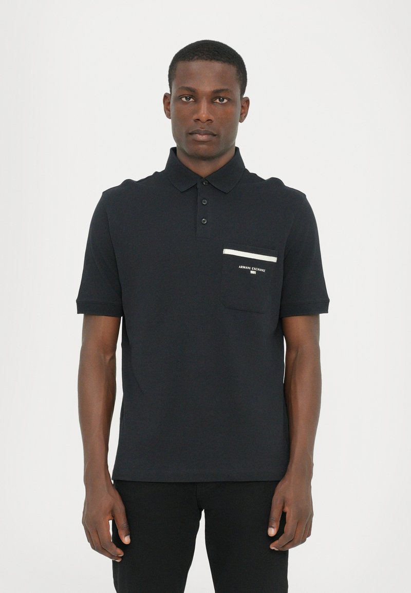 Svart polo skjorte med krage, tre knapper foran og lomme med kontrastfarget hvit stripe. Mykt bomullsstoff med klassisk passform.