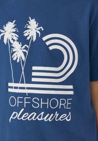 Niebieska bawełniana koszulka z białym wzorem graficznym przedstawiającym palmy oraz napisem "OFFSHORE pleasures". Prosta, nowoczesna i wyrazista w wyglądzie.