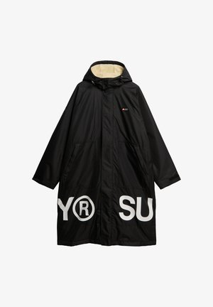 Abrigo negro impermeable con capucha, con un suave forro beige, grandes bolsillos frontales y letras blancas en negrita en el dobladillo.